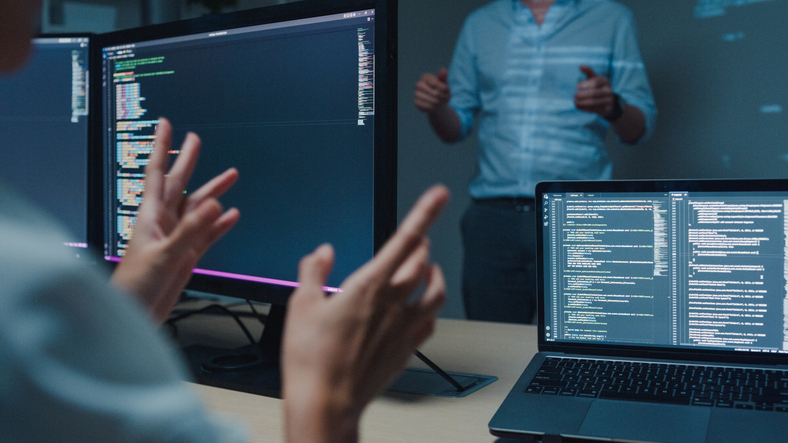 Closeup young Asian man software developers mentor leader manager talking to executive team analyzing source code in office at night. Programmer development concept.