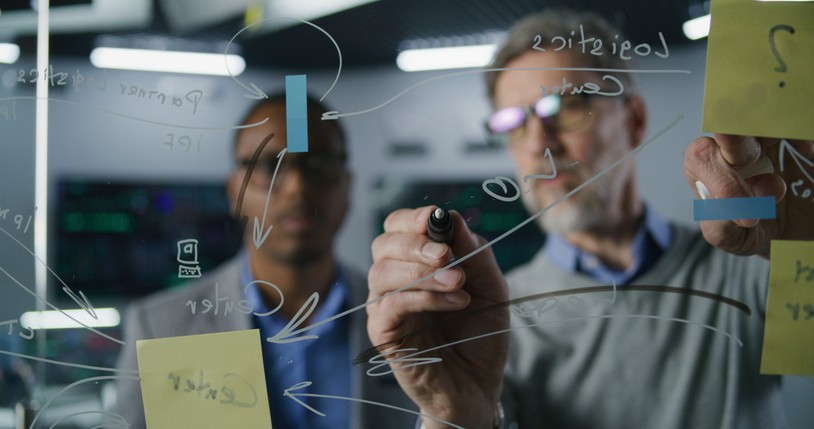 Financial analyst and investment manager draw on glass wall, analyze business strategy, crypto trading in bank office. Computers and digital screens with real-time stocks and exchange market charts.