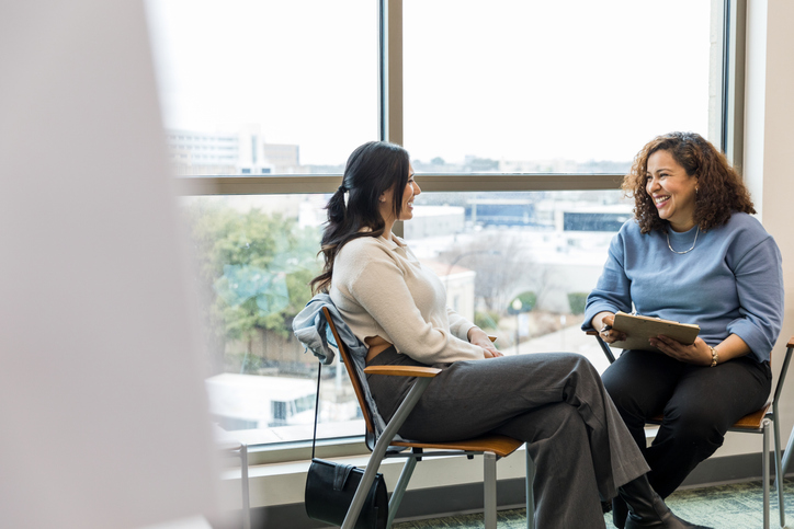 The two businesswomen sit together and enjoy conversation about their recent accomplishments in the last year.