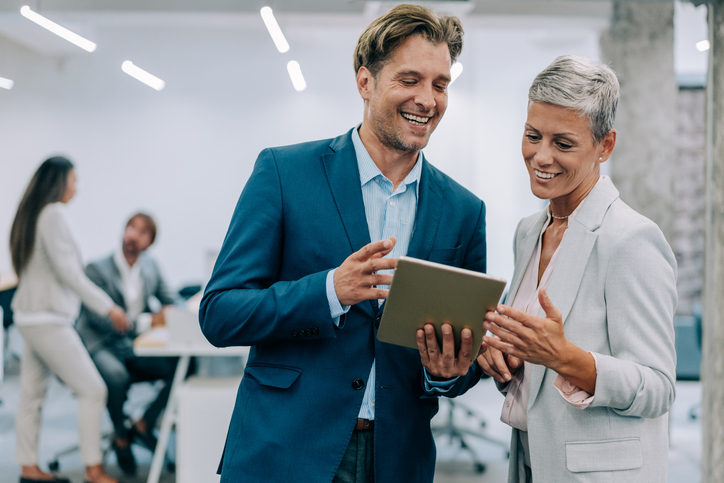 Shot of two coworkers having a discussion in modern office. Businessman and businesswoman in meeting using digital tablet and discussing business strategy. Confident business people working together in the office. Corporate business persons discussing new project and sharing ideas in the workplace.